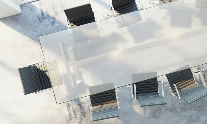 Aerial view of a glass-top conference table surrounded by black chairs in a bright, shadowed room.