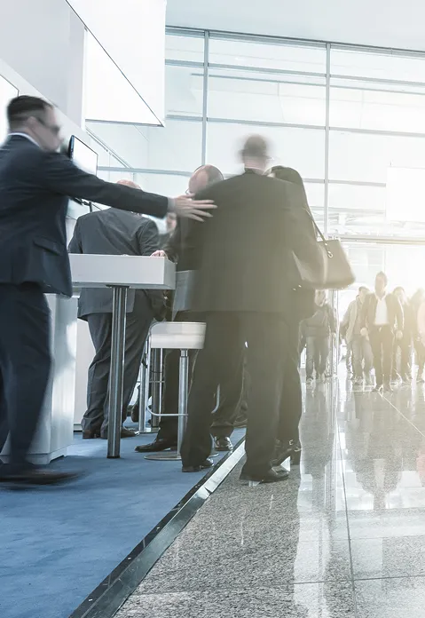 News conference or trade show scene with people in business attire standing and talking in a bright, modern venue.